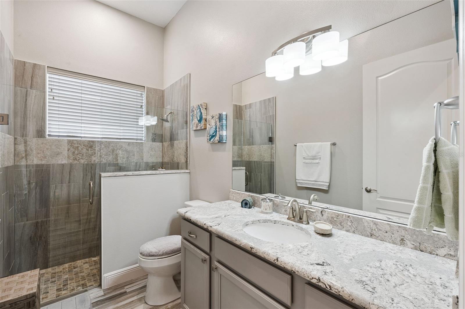 Bathroom 2, situated between bedrooms 2 and 3, features quartz countertops and a zero-entry walk-in shower.