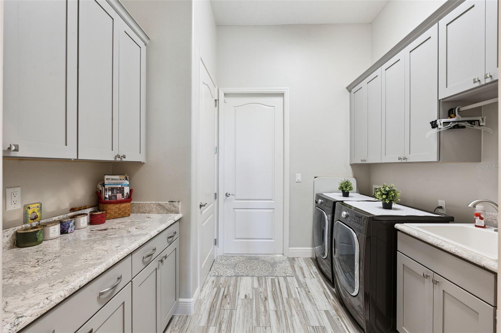 Bright, functional laundry room featuring ample custom cabinetry, a dedicated folding station with a generous quartz countertop, and an undermount utility sink.