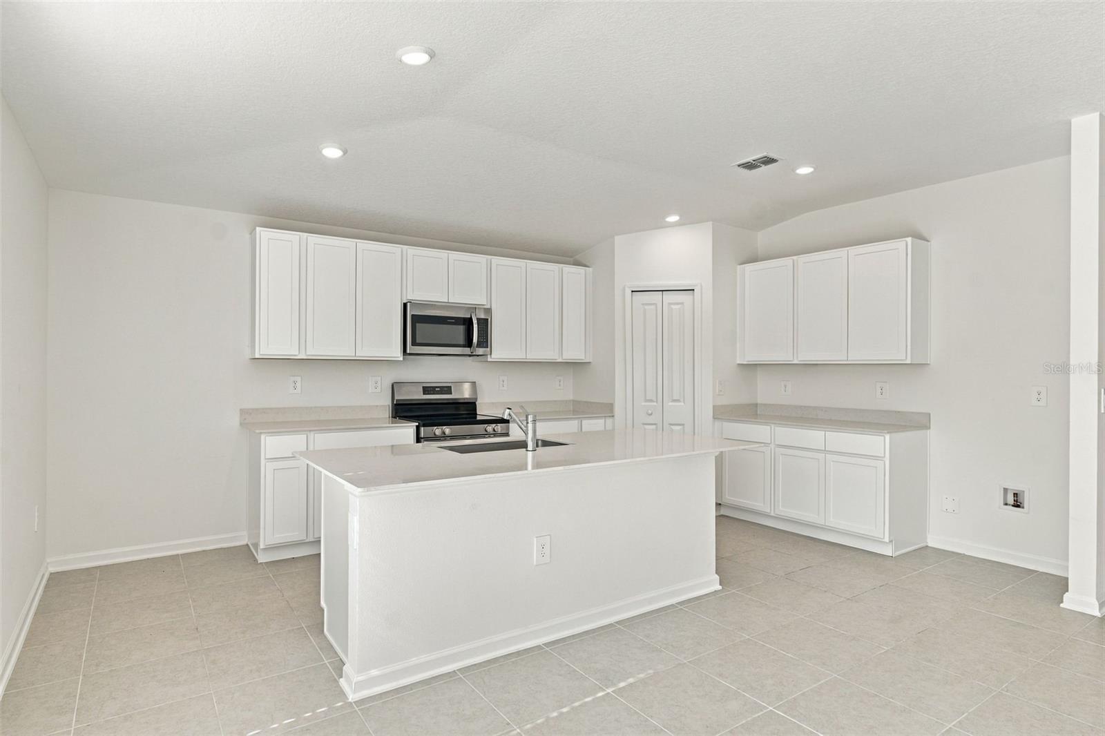The kitchen offers a spacious island with breakfast bar, white Shaker-style cabinetry, and quartz countertops, all overlooking the dining and living areas.