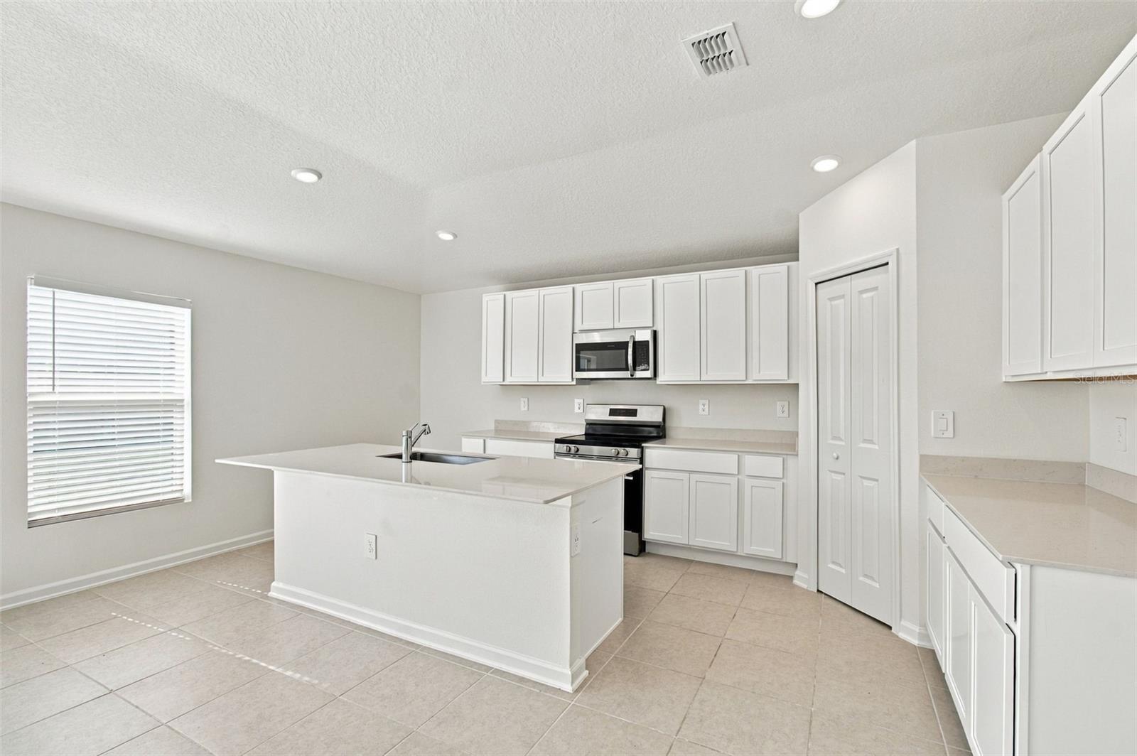The kitchen offers a spacious island with breakfast bar, white Shaker-style cabinetry, and quartz countertops, all overlooking the dining and living areas.