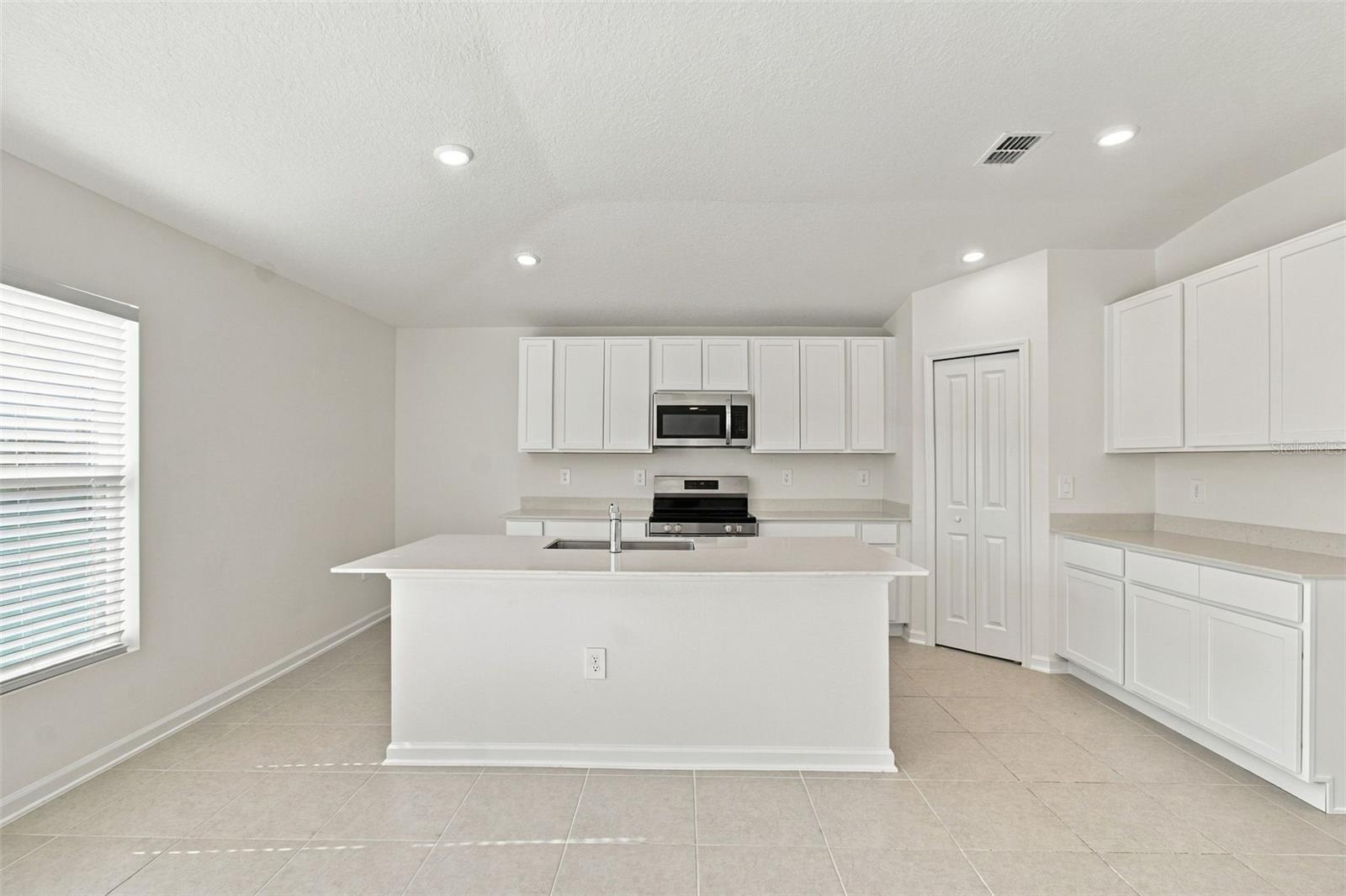 The kitchen offers a spacious island with breakfast bar, white Shaker-style cabinetry, and quartz countertops, all overlooking the dining and living areas.