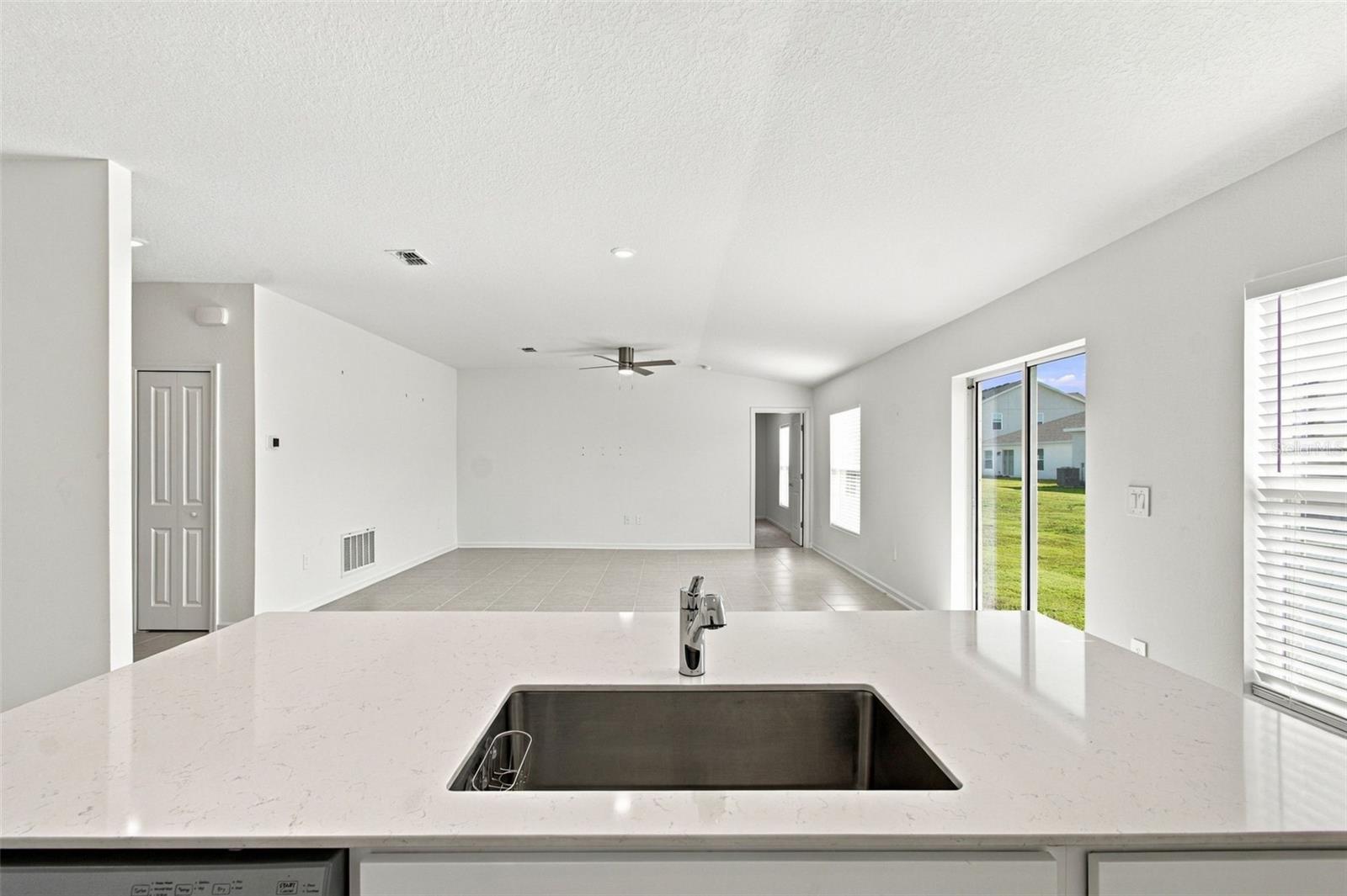 The kitchen offers a spacious island with breakfast bar, white Shaker-style cabinetry, and quartz countertops, all overlooking the dining and living areas.