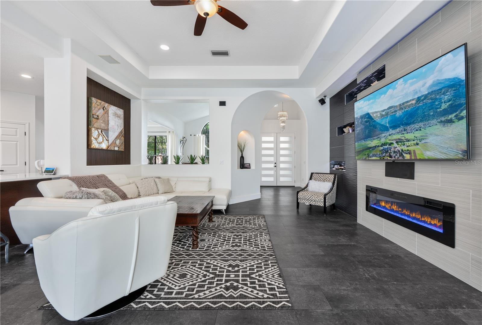 Spacious family room featuring custom wall treatments, recessed display niches with LED lighting and decorative mosaic tile,  and a cozy fireplace.