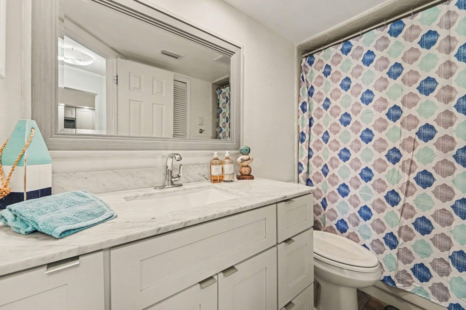 Secondary bathroom with marble-look vanity, spacious mirror, patterned shower curtain