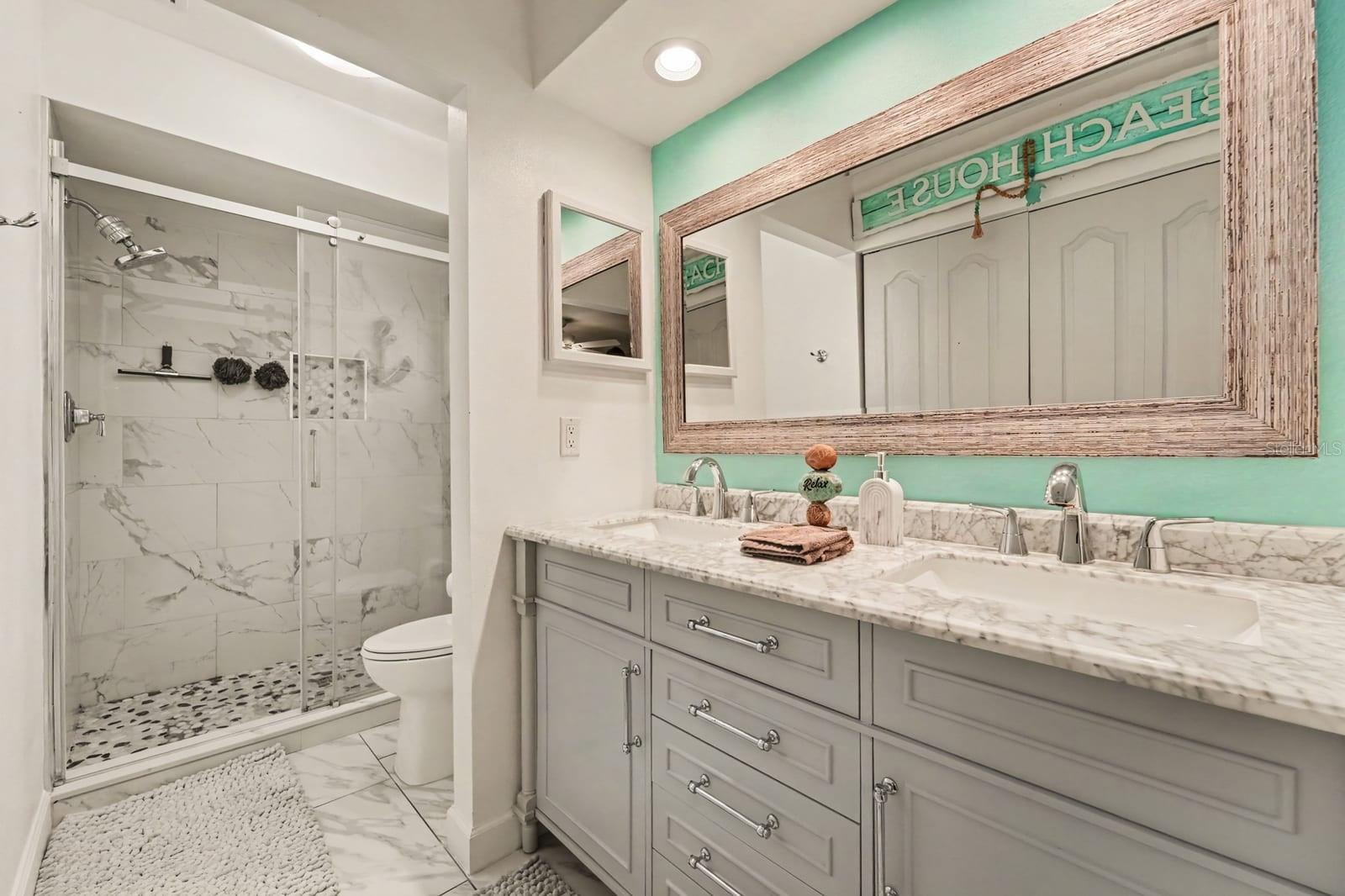 Primary bath features walk-in shower with marble tile, frameless glass enclosure
