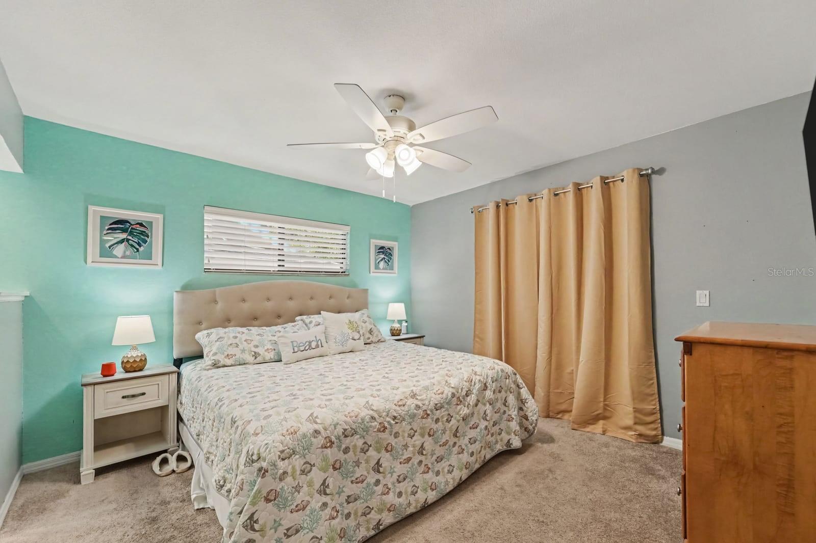 Turquoise accent wall and tufted headboard create a bright, coastal-inspired primary bedroom