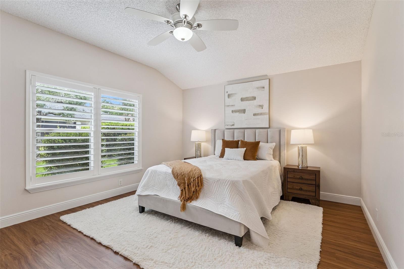 15'6" x 12'6" Primary Bedroom w/ a laminate floor, ceiling fan & Plantation style shutters