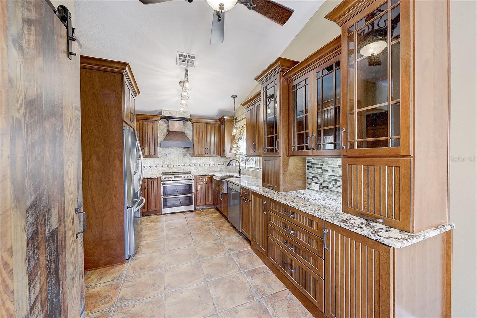 The custom-renovated kitchen, completed in 2021, is a standout feature, offering custom cabinetry with soft-close doors and drawers, polished granite countertops with natural edges, a custom tile backsplash, a copper undermount sink, and a touch-operated faucet with an integrated pot-filler feature. Additional details include a solid-wood barn door pantry, a built-in cabinet with antique glass doors and interior lighting, under-cabinet lighting, and quality appliances, including a French-door refrigerator, extra-quiet Bosch dishwasher, microwave installed in the lower cabinetry, and LG double oven, complemented by a full-size copper overhead range exhaust hood.