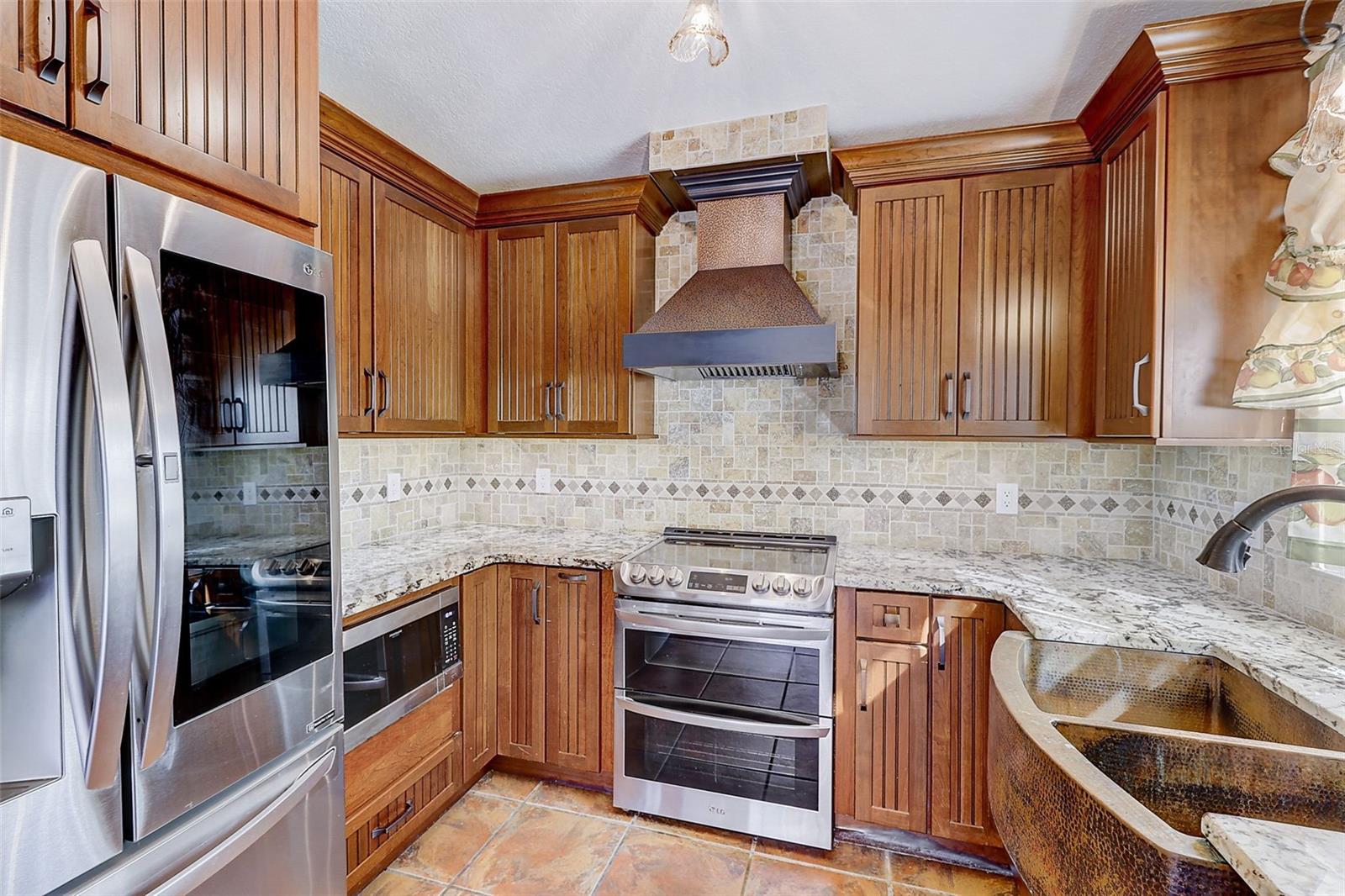 The custom-renovated kitchen, completed in 2021, is a standout feature, offering custom cabinetry with soft-close doors and drawers, polished granite countertops with natural edges, a custom tile backsplash, a copper undermount sink, and a touch-operated faucet with an integrated pot-filler feature. Additional details include a solid-wood barn door pantry, a built-in cabinet with antique glass doors and interior lighting, under-cabinet lighting, and quality appliances, including a French-door refrigerator, extra-quiet Bosch dishwasher, microwave installed in the lower cabinetry, and LG double oven, complemented by a full-size copper overhead range exhaust hood.