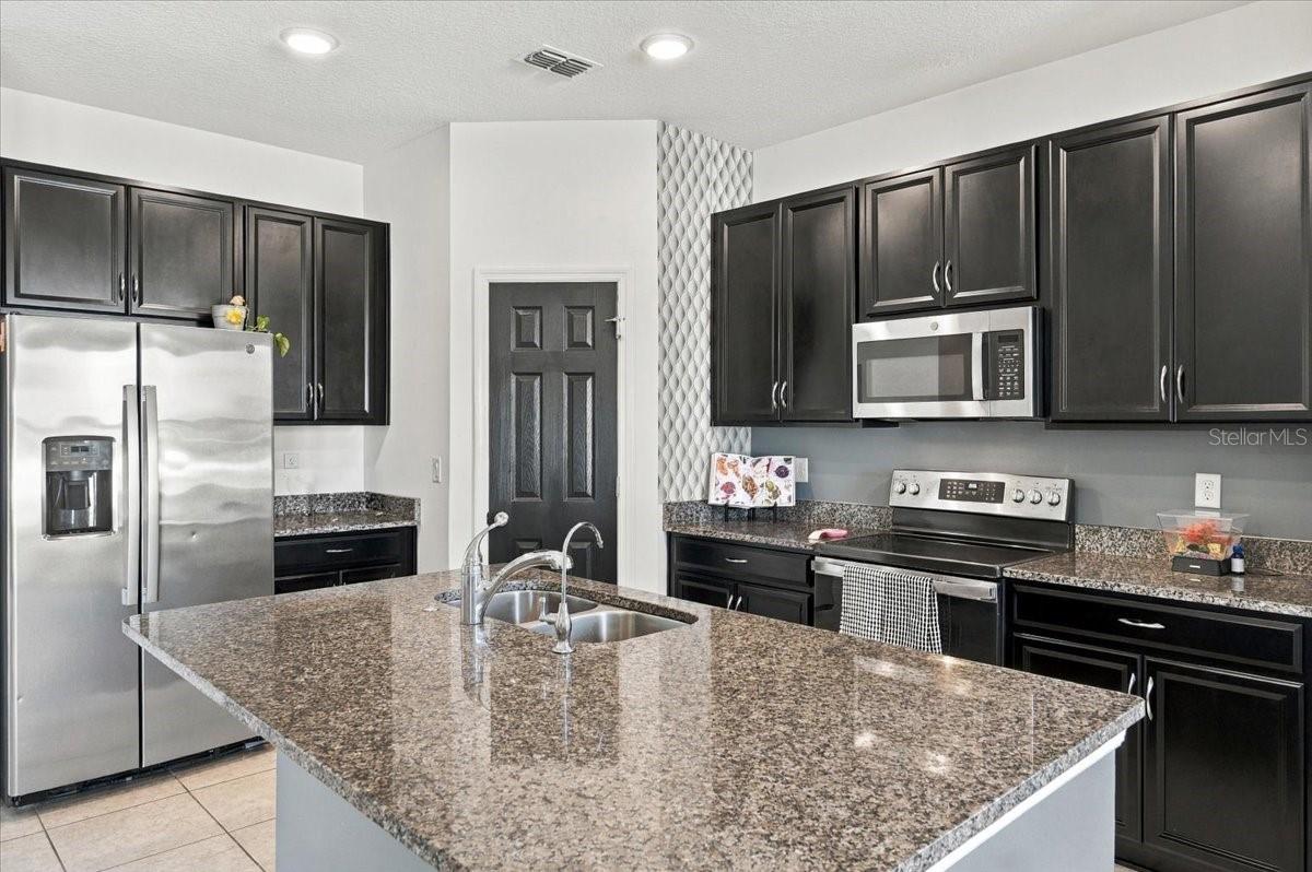 Spacious kitchen featuring granite countertops, dark cabinetry, stainless steel appliances, and a large center island. Spacious kitchen featuring granite countertops, dark cabinetry, stainless steel appliances, and a large center island.