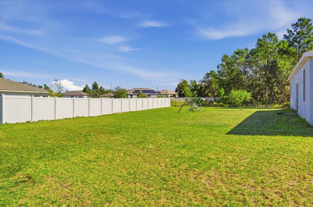 Expansive backyard featuring a large grassy area and white privacy fencing along one side of the property.