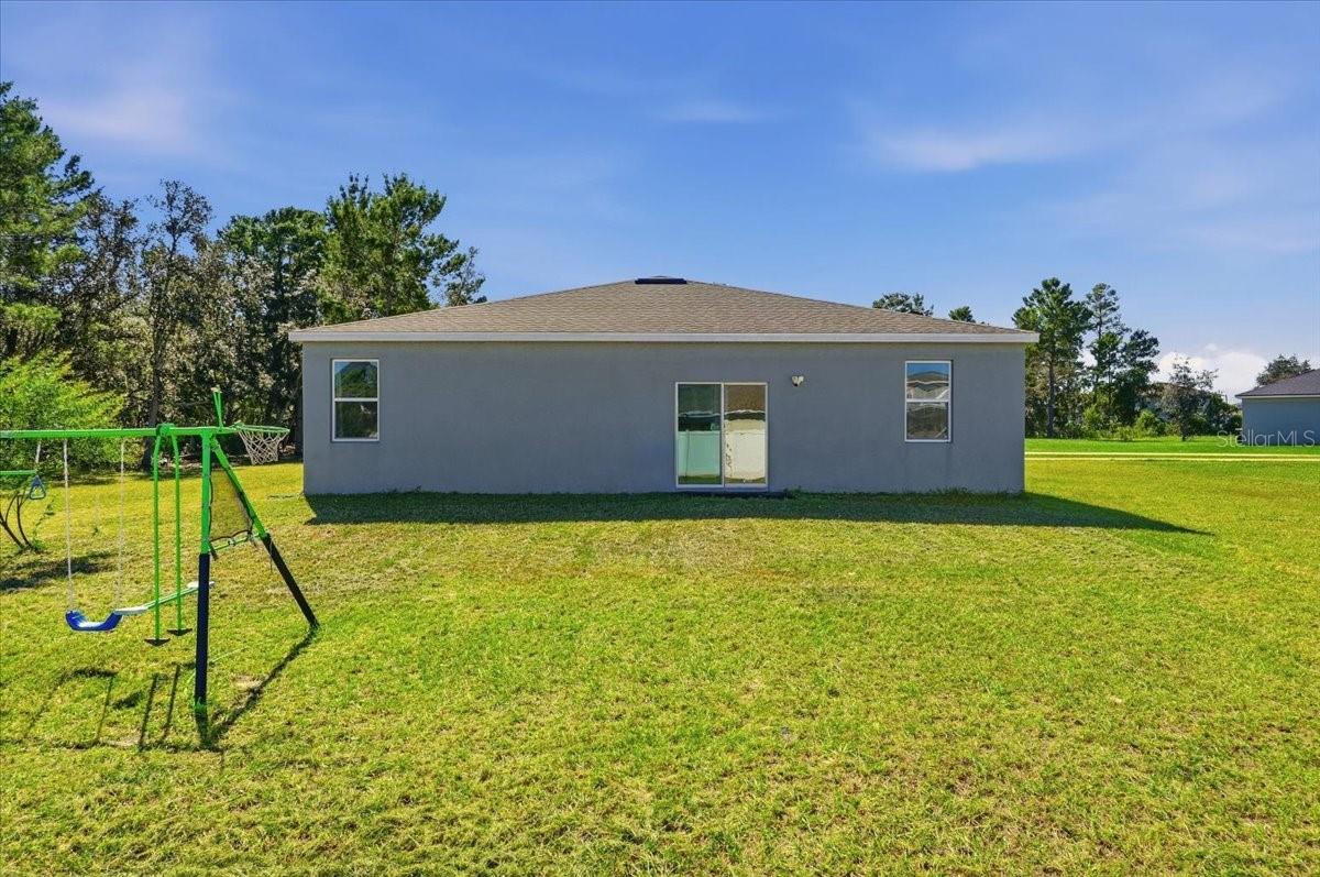 Rear view of the home showcasing the expansive backyard and open lawn with plenty of room to enjoy the outdoors.