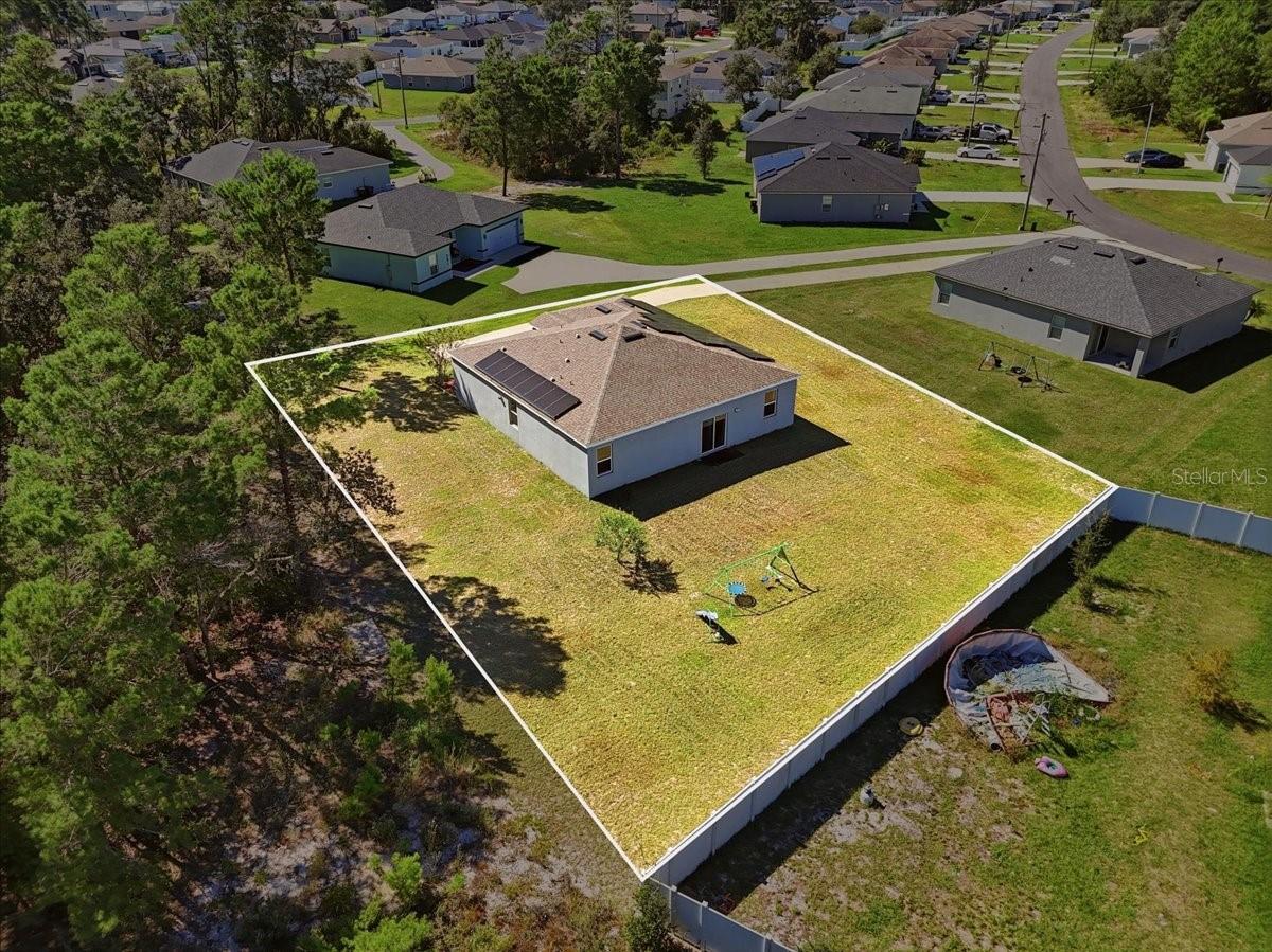 Elevated aerial perspective highlighting the spacious backyard, open green space, and surrounding properties.