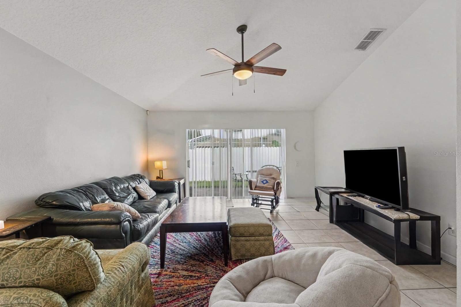 Spacious living area with vaulted ceiling, tile flooring, and sliding glass patio doors Spacious living area with vaulted ceiling, tile flooring, and sliding glass patio doors