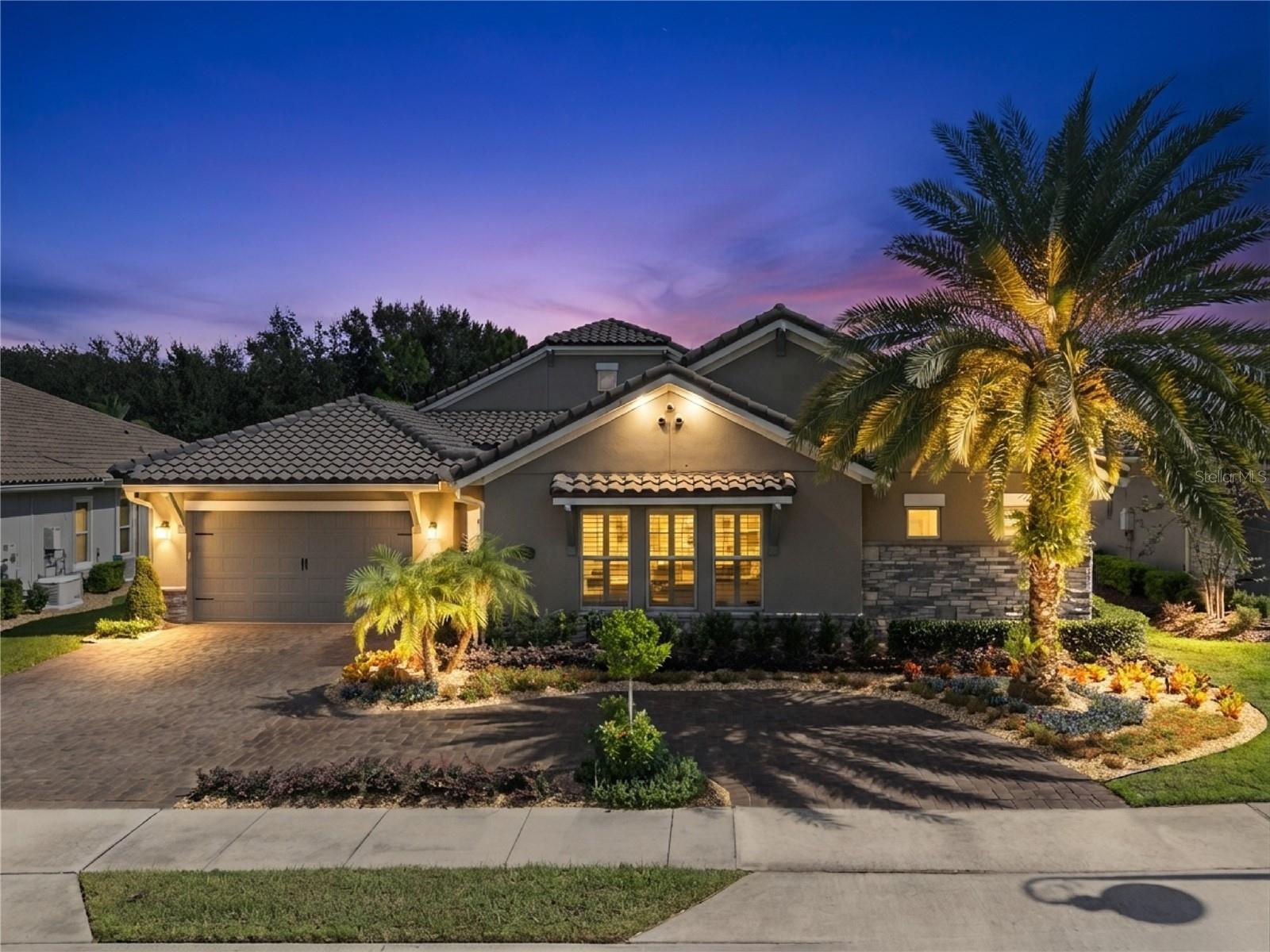 Elegant, Mediterranean-inspired exterior w/ tile roof, paver driveway, lush tropical landscaping and a gated courtyard entrance