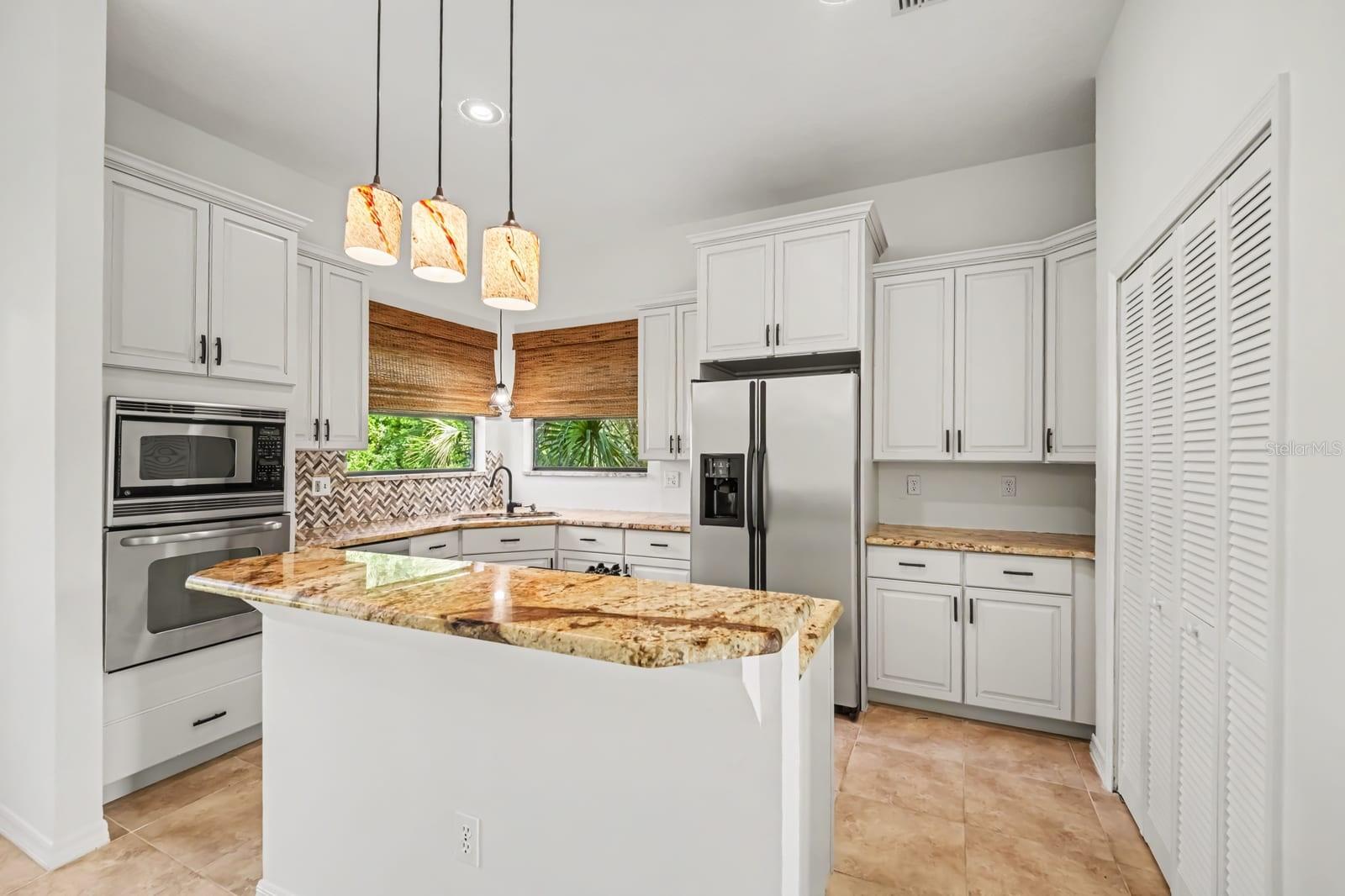 Chef's Kitchen Featuring Granite Island, White Cabinetry & Integrated Appliances