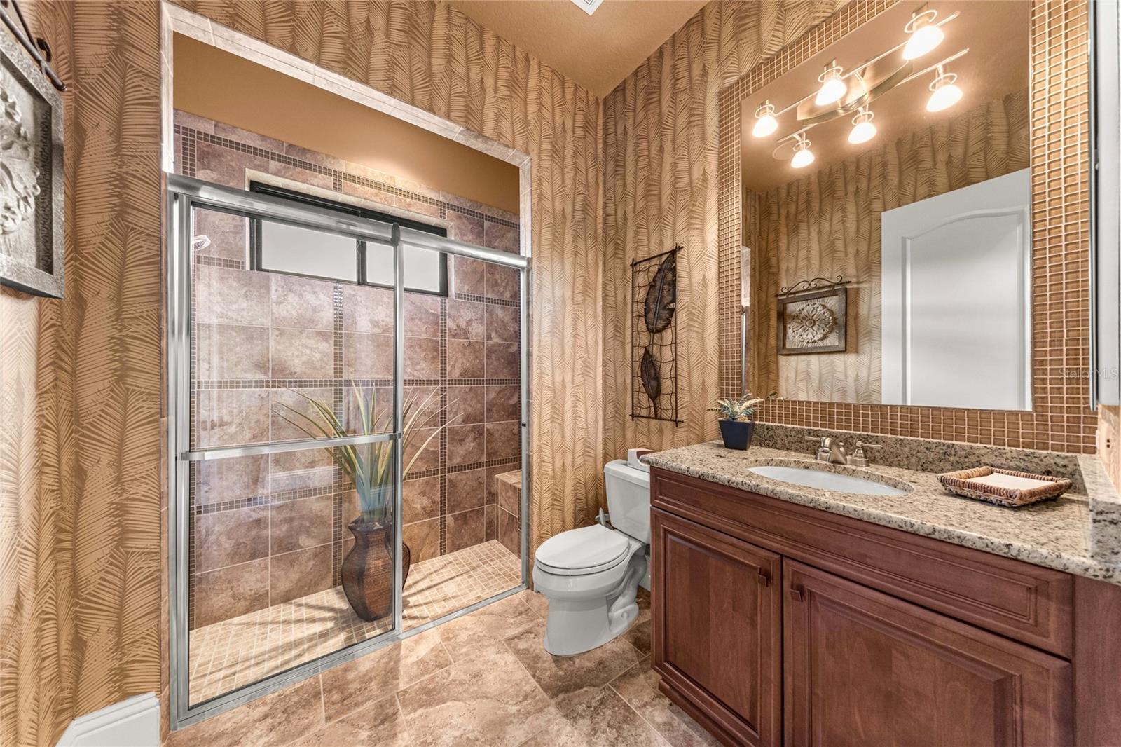 Attractive bathroom featuring granite countertops, wood cabinetry, decorative wall finishes, and natural light.
