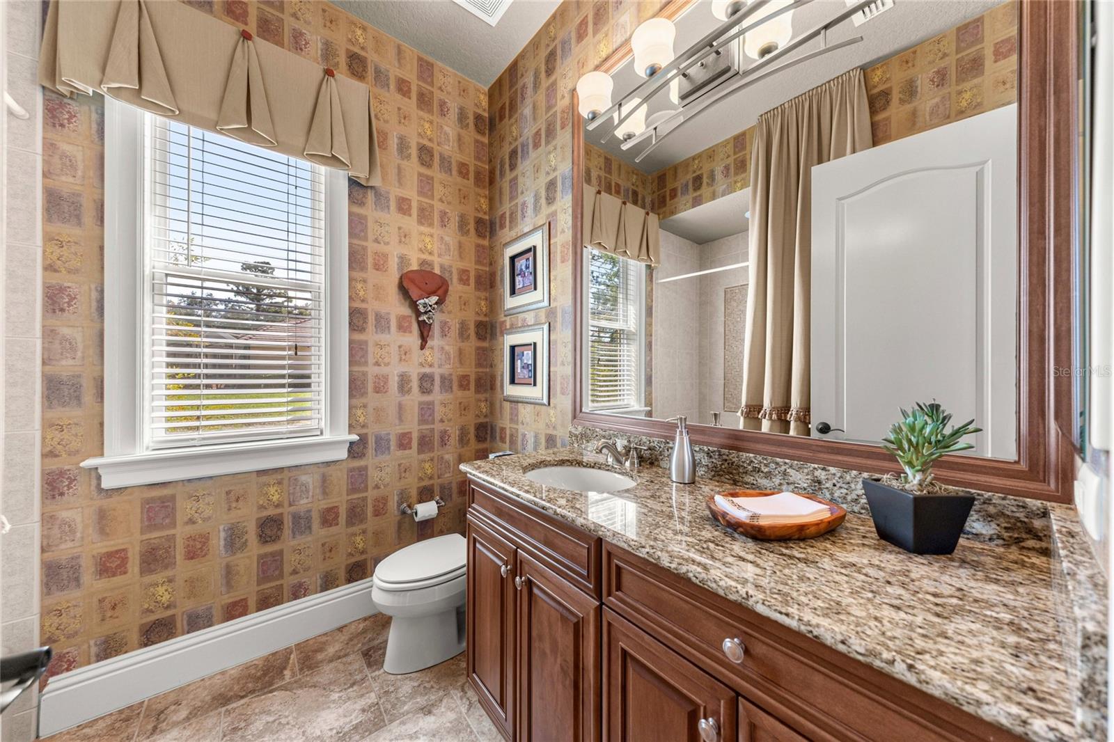 Attractive bathroom featuring granite countertops, wood cabinetry, decorative wall finishes, and natural light.