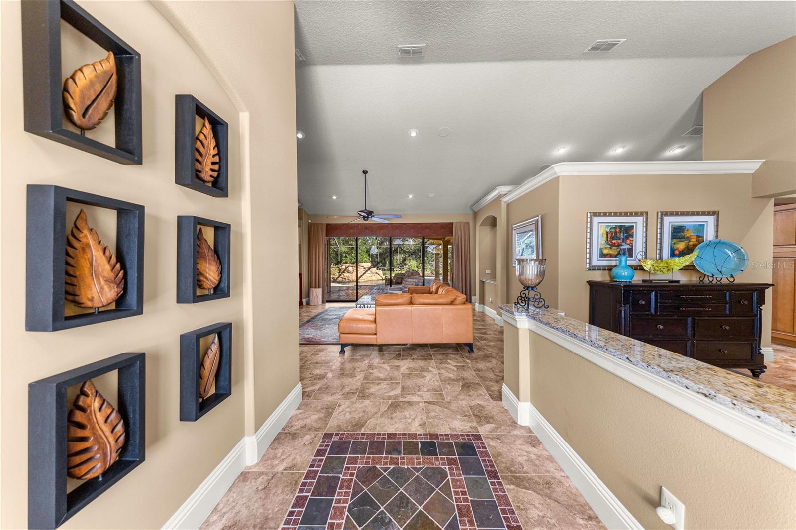 Welcoming foyer featuring decorative tile flooring, high ceilings, elegant crown molding, and an open view into the spacious living area with sliding glass doors overlooking the screened outdoor retreat. Welcoming foyer featuring decorative tile flooring, high ceilings, elegant crown molding, and an open view into the spacious living area with sliding glass doors overlooking the screened outdoor retreat.