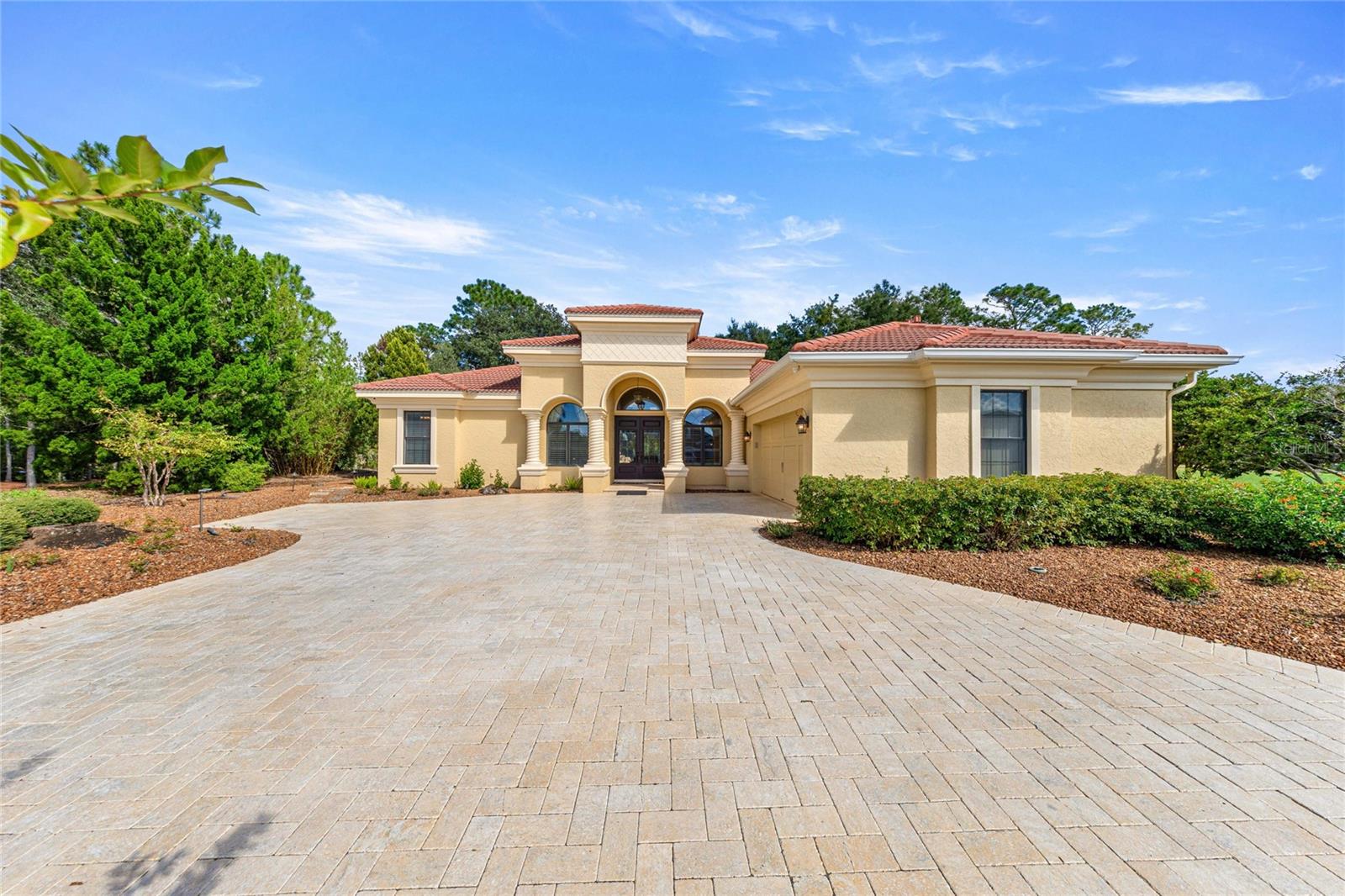 Beautiful Mediterranean-inspired home featuring a tile roof, elegant architectural detailing, grand covered entrance, and expansive paver driveway.