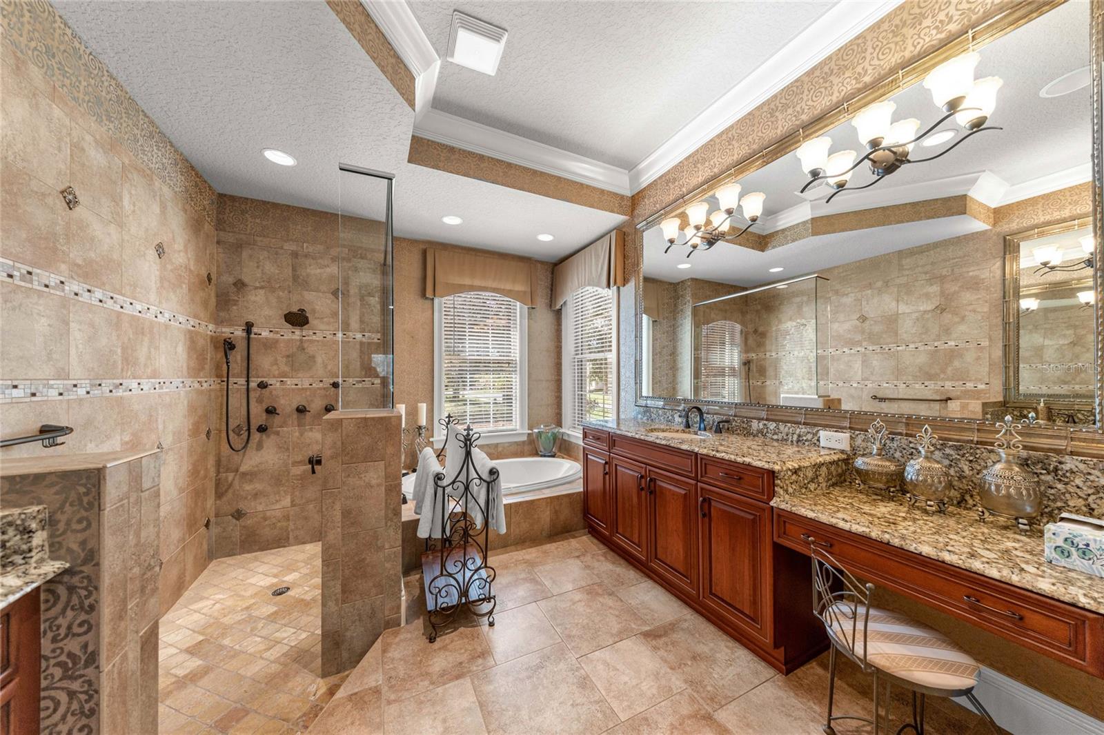 Luxurious owner's bathroom with granite countertops, custom cabinetry, spacious walk-in shower, and soaking tub.