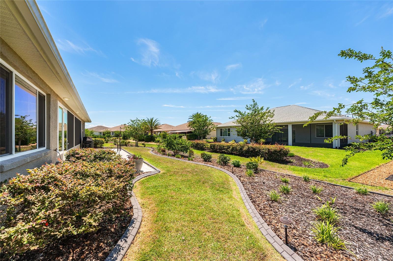 Beautifully landscaped backyard featuring attractive concrete curbing, established shrubs, colorful plantings, and a lush green lawn. Thoughtfully designed landscape beds enhance the outdoor setting and create an inviting space to enjoy Florida living.