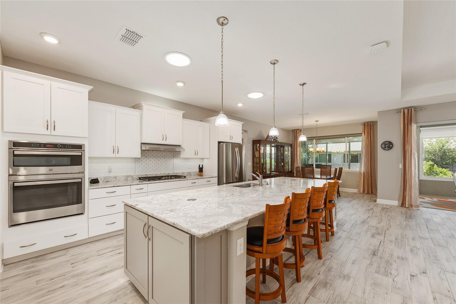 Beautifully appointed kitchen featuring an expansive Cambria quartz island with seating, staggered cabinetry, stainless steel appliances, GE double convection ovens with microwave, and two solar tubes that fill the space with natural light.