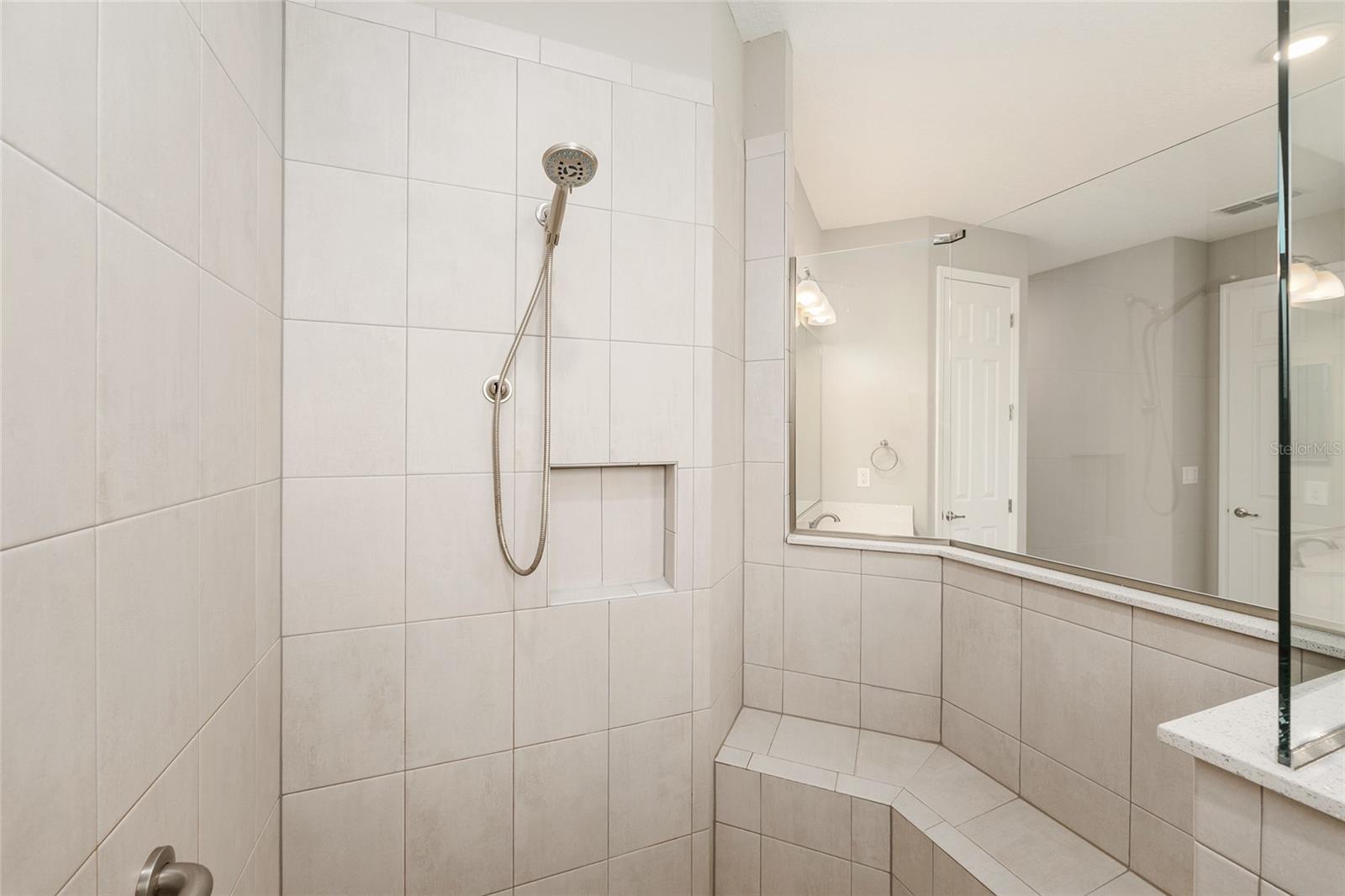 Closer view of the first primary suite's beautifully tiled shower, showcasing the integrated corner bench and thoughtfully designed space for added comfort and convenience.
