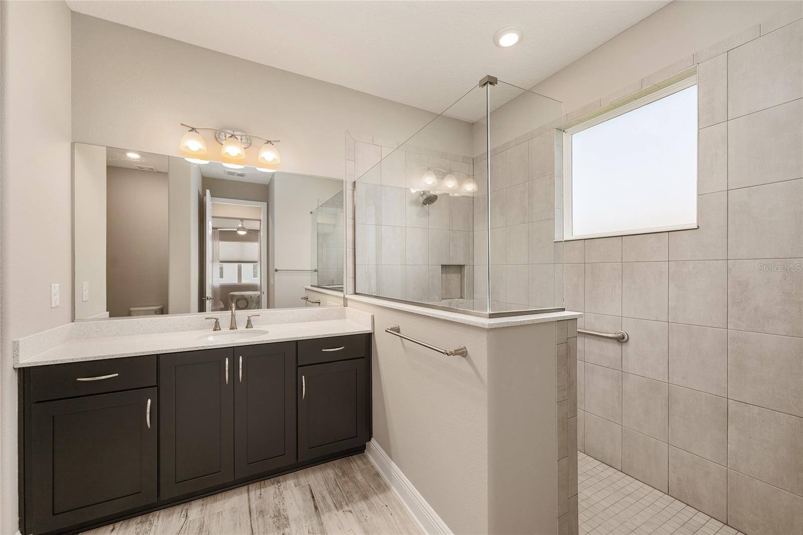 Second primary ensuite bathroom showcasing a spacious zero-entry walk-in shower with a glass enclosure, tiled walls, built-in niche, and natural light from the privacy window.
