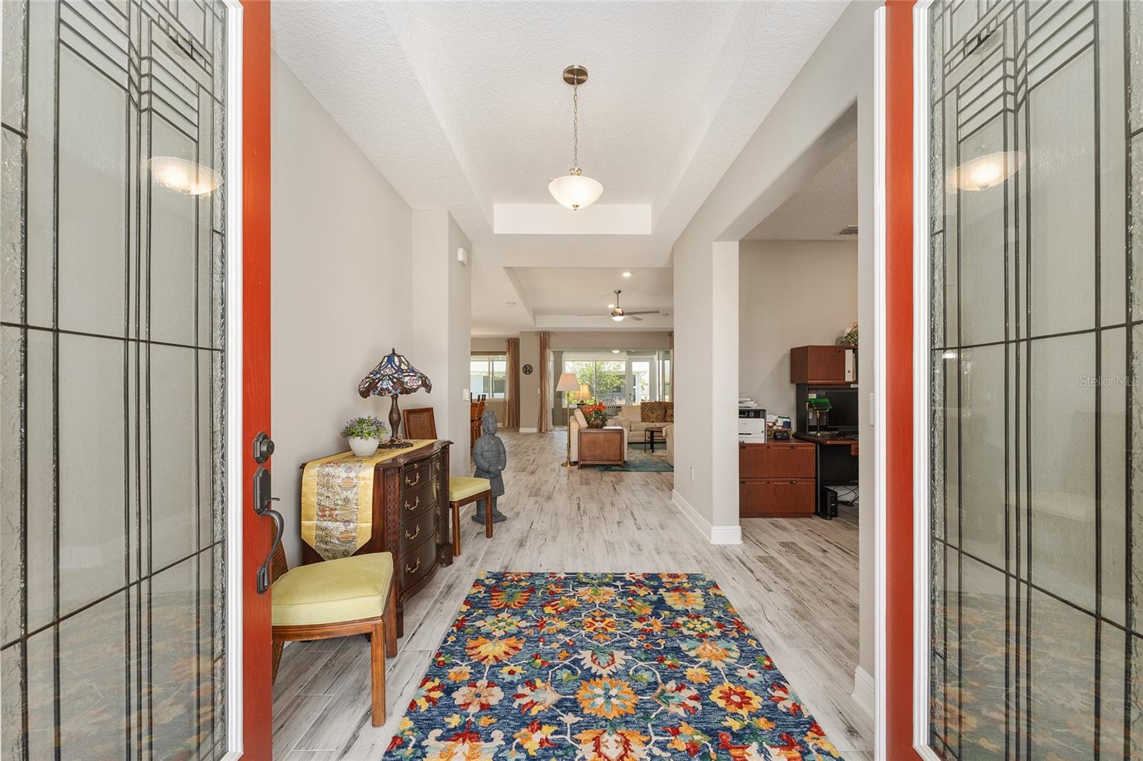Inviting foyer featuring elegant leaded-glass double entry doors, a decorative tray ceiling, and ceramic plank flooring, creating a bright and welcoming introduction to the home.