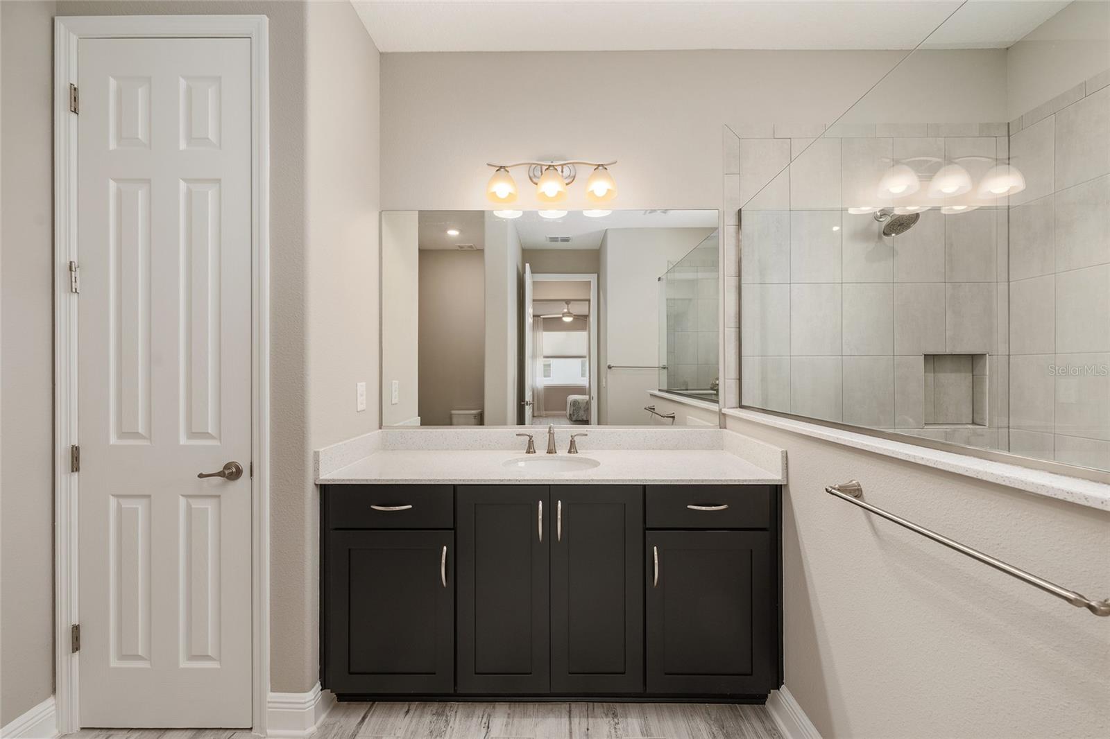 Second primary suite's private ensuite bathroom features a spacious vanity with a light-colored countertop, rich espresso cabinetry, generous storage, a large mirror, and a convenient linen closet.