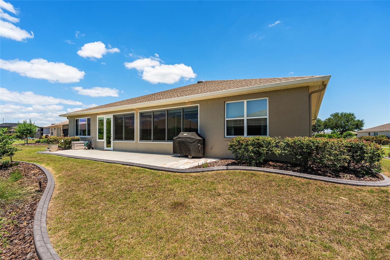 Full rear view of the home showcasing the expansive patio, enclosed lanai, and beautifully maintained landscaping. The generous backyard provides plenty of open space to relax and enjoy the Florida lifestyle.