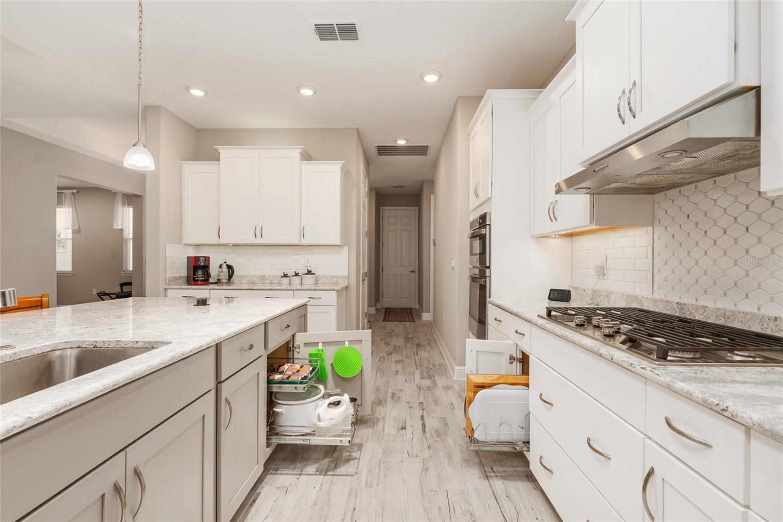 Thoughtfully designed kitchen featuring a large single-basin sink with built-in soap dispenser, convenient pull-out storage organizers, Cambria quartz countertops, and a decorative tile backsplashcombining functionality with everyday convenience.