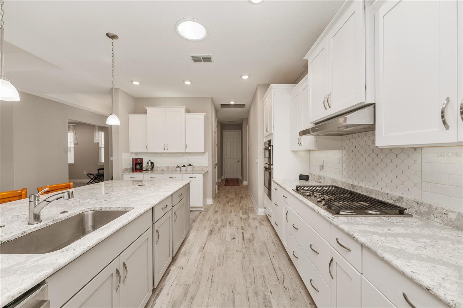 Beautifully designed kitchen featuring staggered cabinetry, Cambria quartz countertops, a decorative tile backsplash, GE five-burner gas cooktop, over- and under-cabinet lighting, switched outlets above the cabinets, ceramic plank flooring, recessed lighting, and an open layout connecting to the dining and great room.