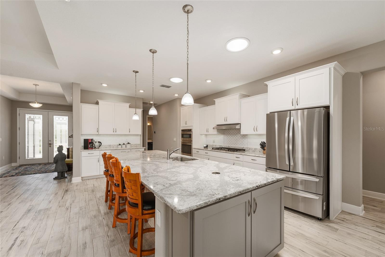 Beautifully appointed kitchen featuring staggered cabinetry, convenient pull-out drawers, a neutral tile backsplash, and two solar tubes that fill the space with natural light. GE gas range, GE dishwasher, and LG refrigerator complement the impressive 12' x 4.5' Cambria quartz island, complete with pop-up outlets and abundant additional storage.