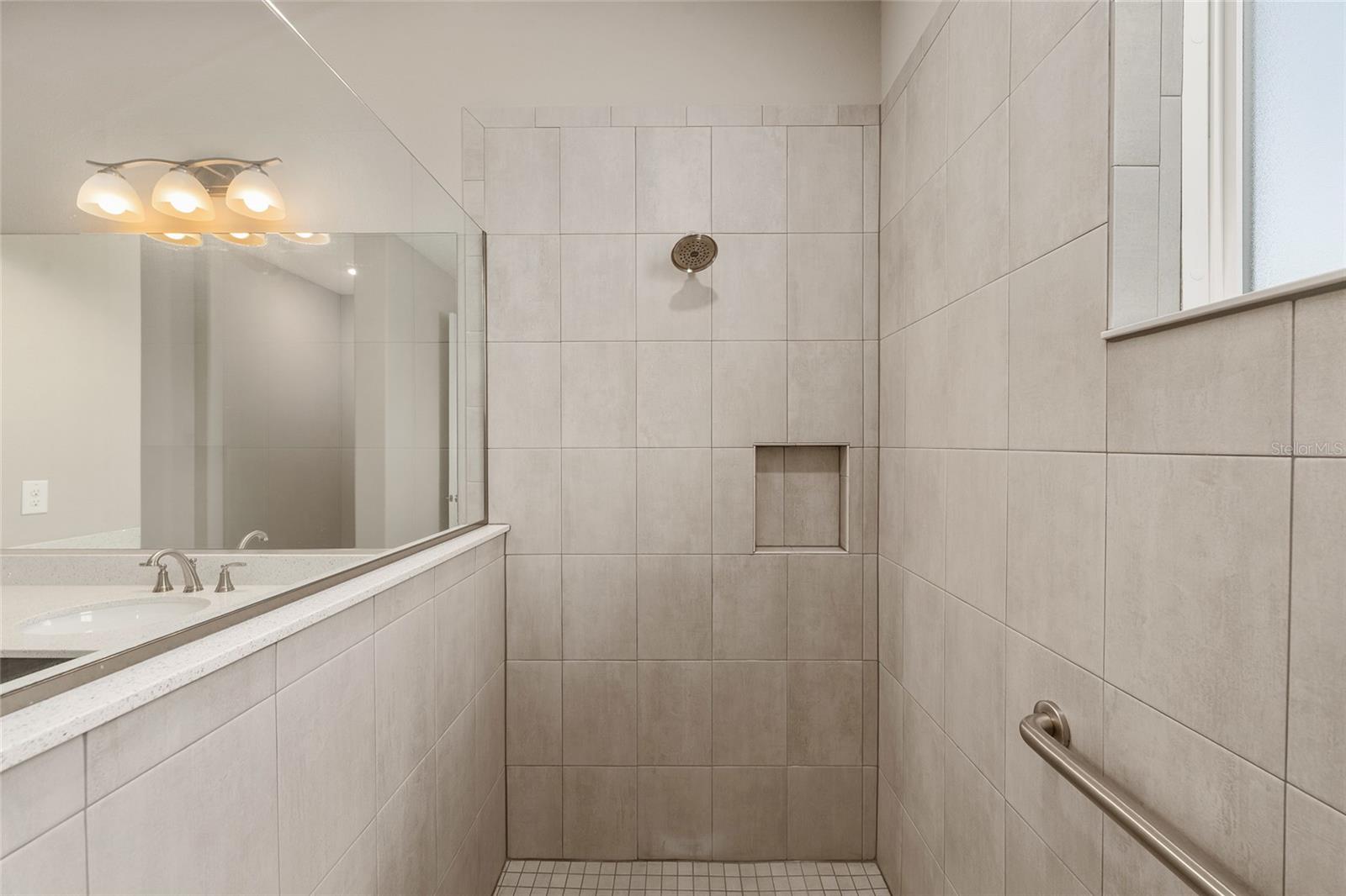 Closer view of the second primary ensuite shower, highlighting the built-in toiletry niche, conveniently positioned grab bar, and coordinating tile finishes for added functionality and comfort.