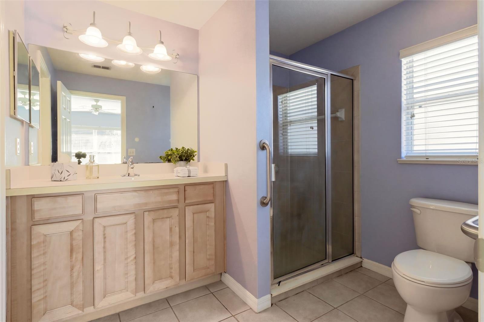 The en-suite primary bathroom is designed for comfort, featuring a comfort-height vanity, tile flooring, and a walk-in shower with a glass door.