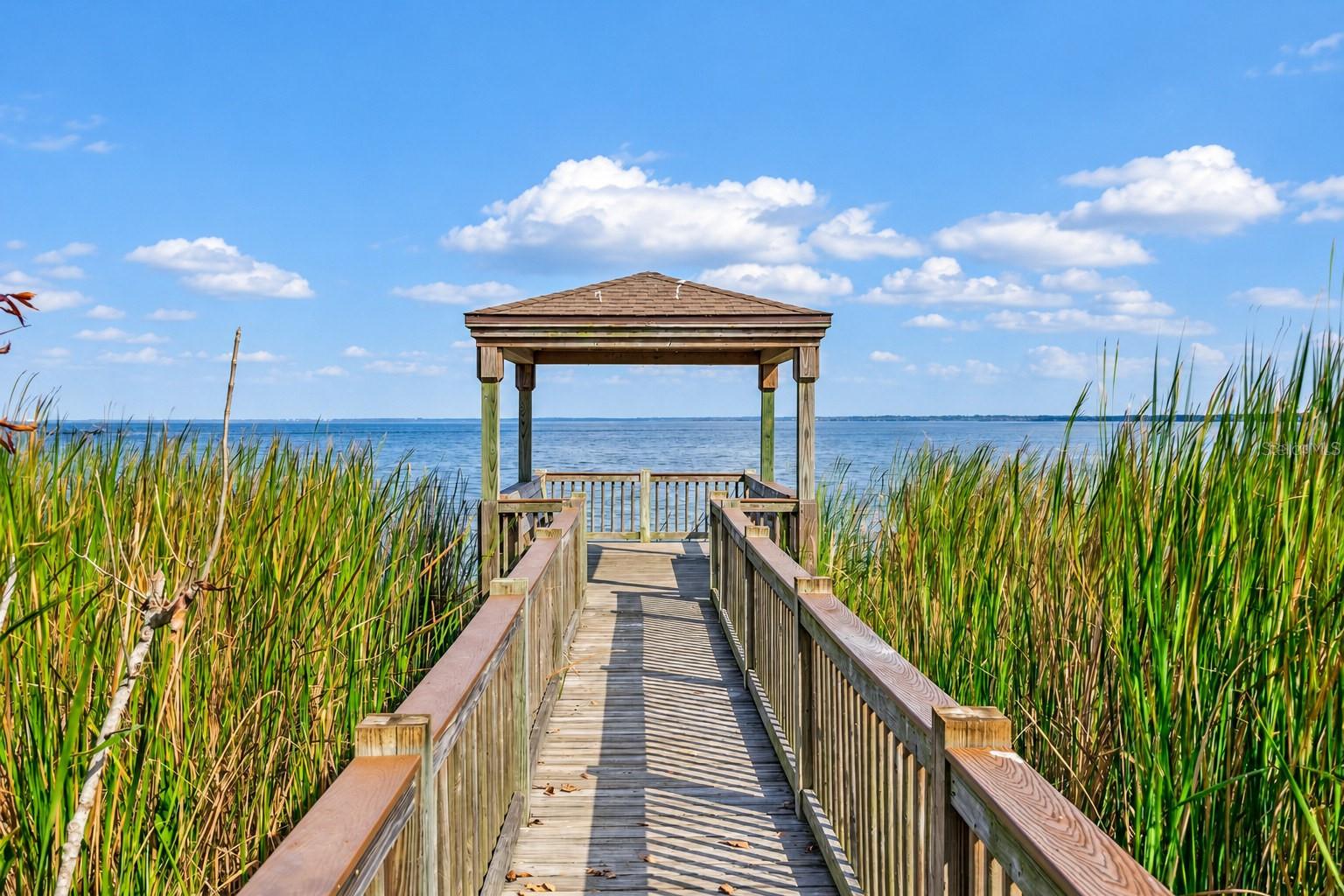 Community boardwalk leading to a covered lakeside gazebo with sweeping water views.