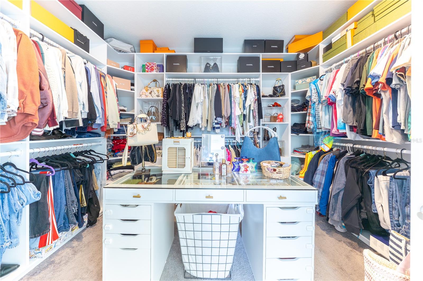 Expansive custom walk-in closet with built-in shelving, double hanging rods, and a central glass-top storage island.