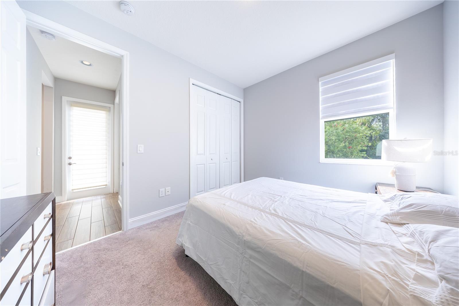 Bedroom with soft neutral tones, carpet flooring, a closet with folding doors, and a window overlooking greenery.