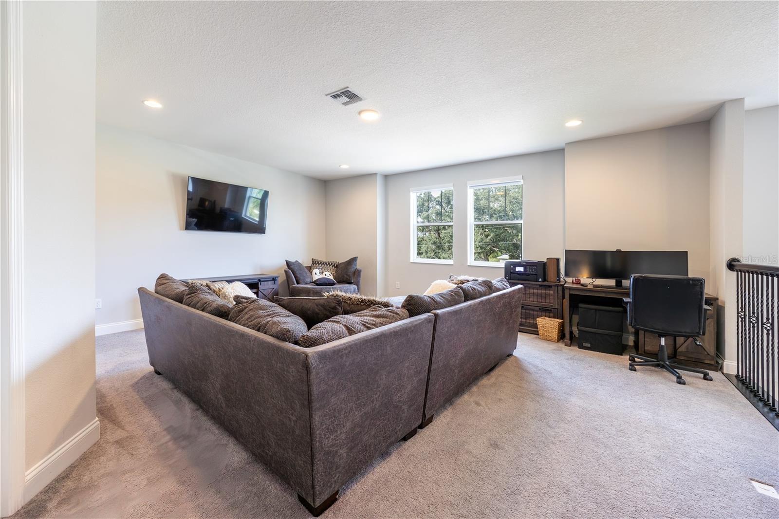 Versatile upstairs loft with spacious seating and a home office area overlooking the trees.