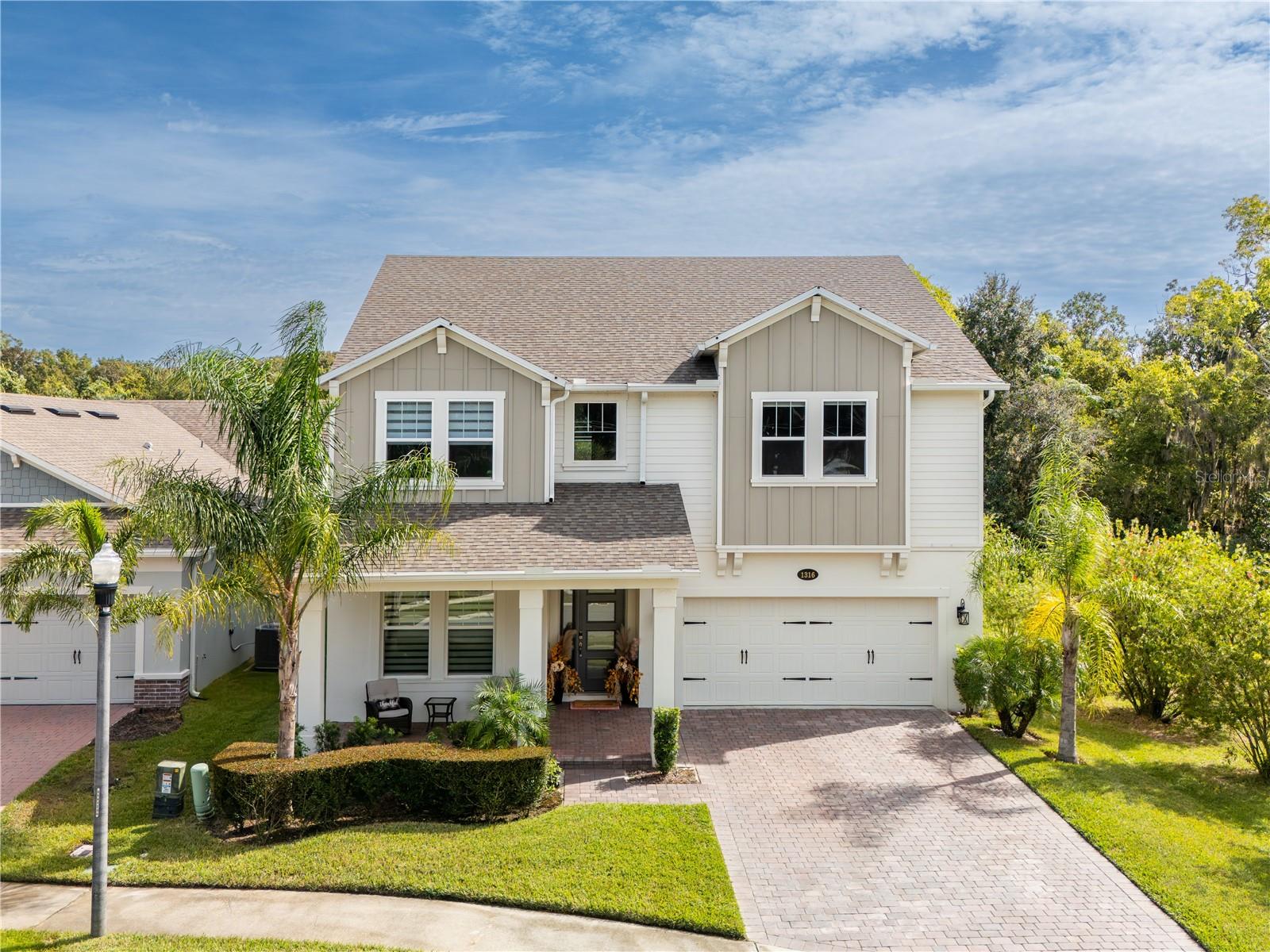 Elegant two-story home with a covered front porch, paver driveway, and tropical landscaping.