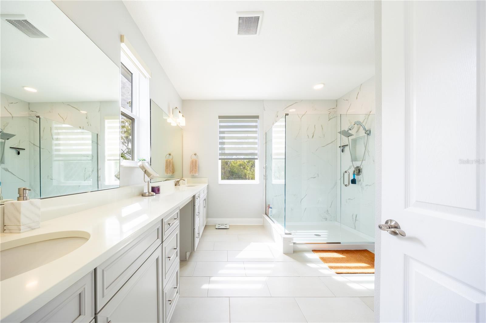 Spacious primary bathroom with a dual-sink vanity, makeup area, and frameless glass shower.