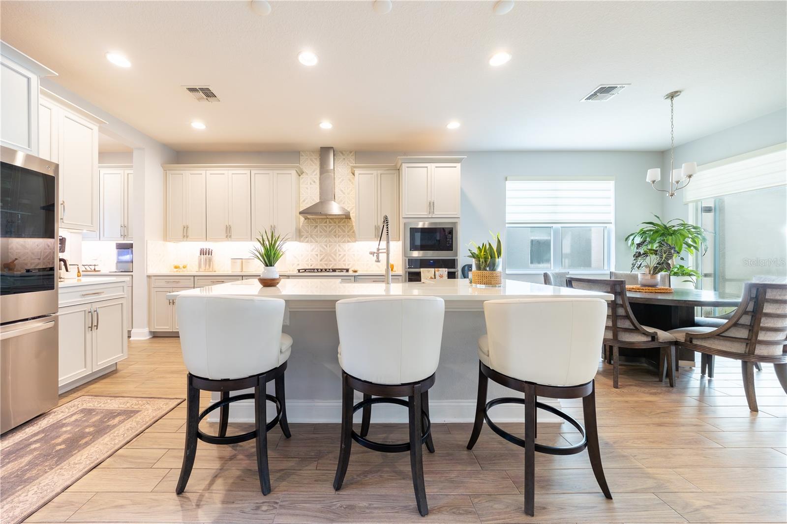 Spacious kitchen island with seating for three, complemented by white cabinetry and a decorative tile backsplash.