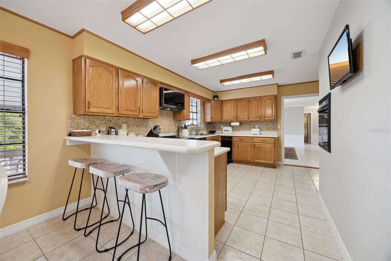 Kitchen Breakfast Bar: Spacious kitchen area showcasing a raised breakfast bar peninsula with stool seating, warm wood cabinetry, and mosaic tile backsplash.
