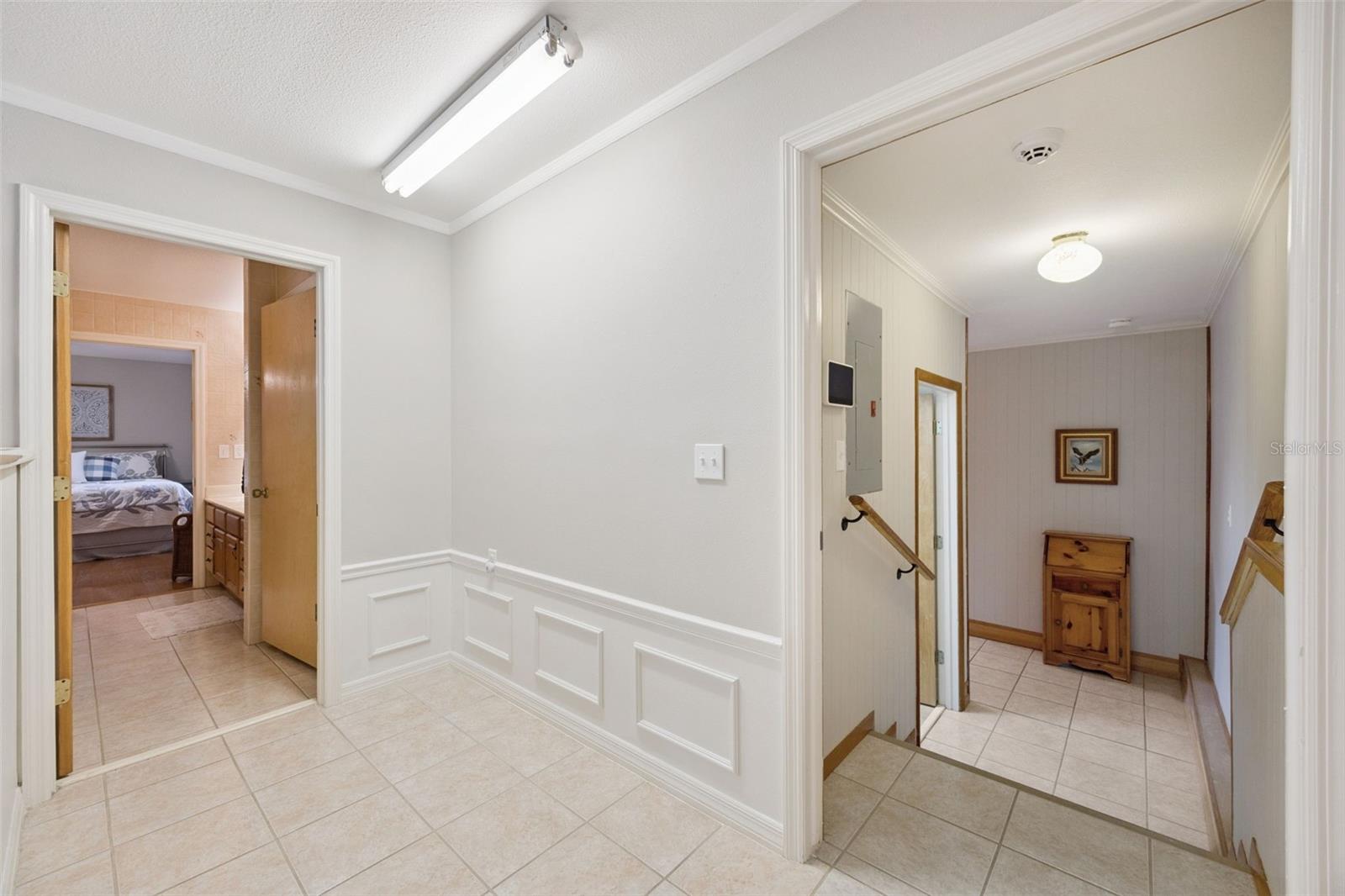 Split-Level Hallway Landing: Tiled split-level transition area featuring lower-level stair access, wainscoting wall detail, overhead lighting, and bedroom doorways.