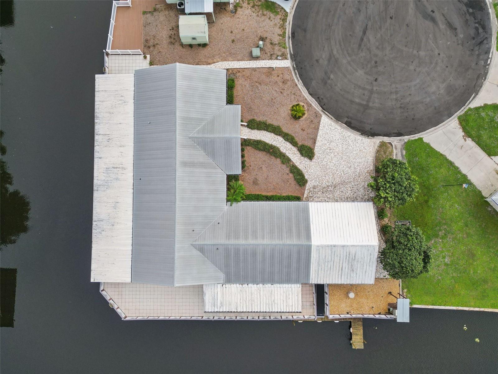 Aerial Top-Down View: Overhead drone shot highlighting the property layout, metal roof, cul-de-sac positioning, and canal wrap-around.