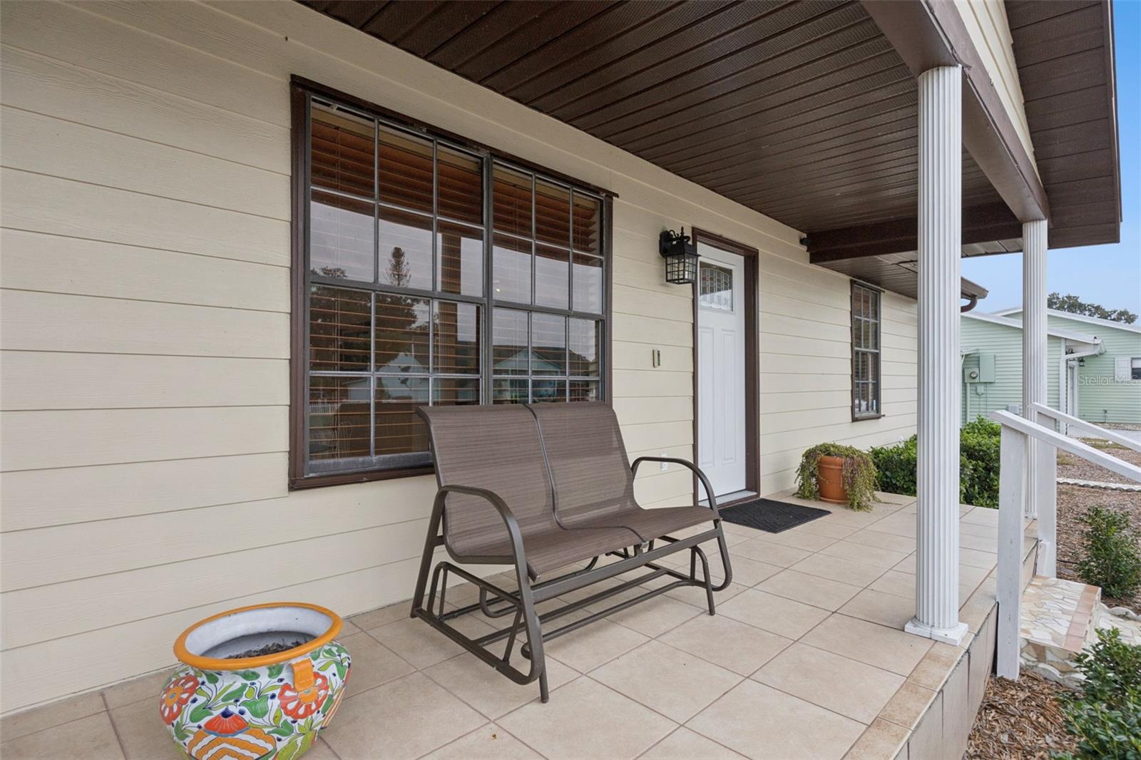 Porch Seating Area: Cozy front porch retreat with tiled floor, dark wood panel ceiling, and ample space for outdoor seating.