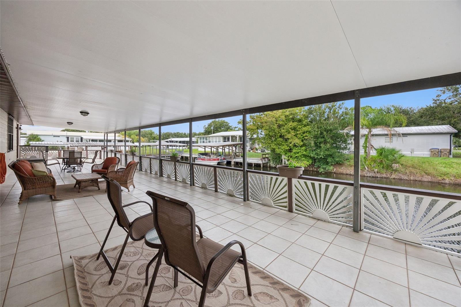 Covered Waterfront Patio: Expansive covered rear patio with tile flooring, decorative railing, and serene views overlooking the canal water.