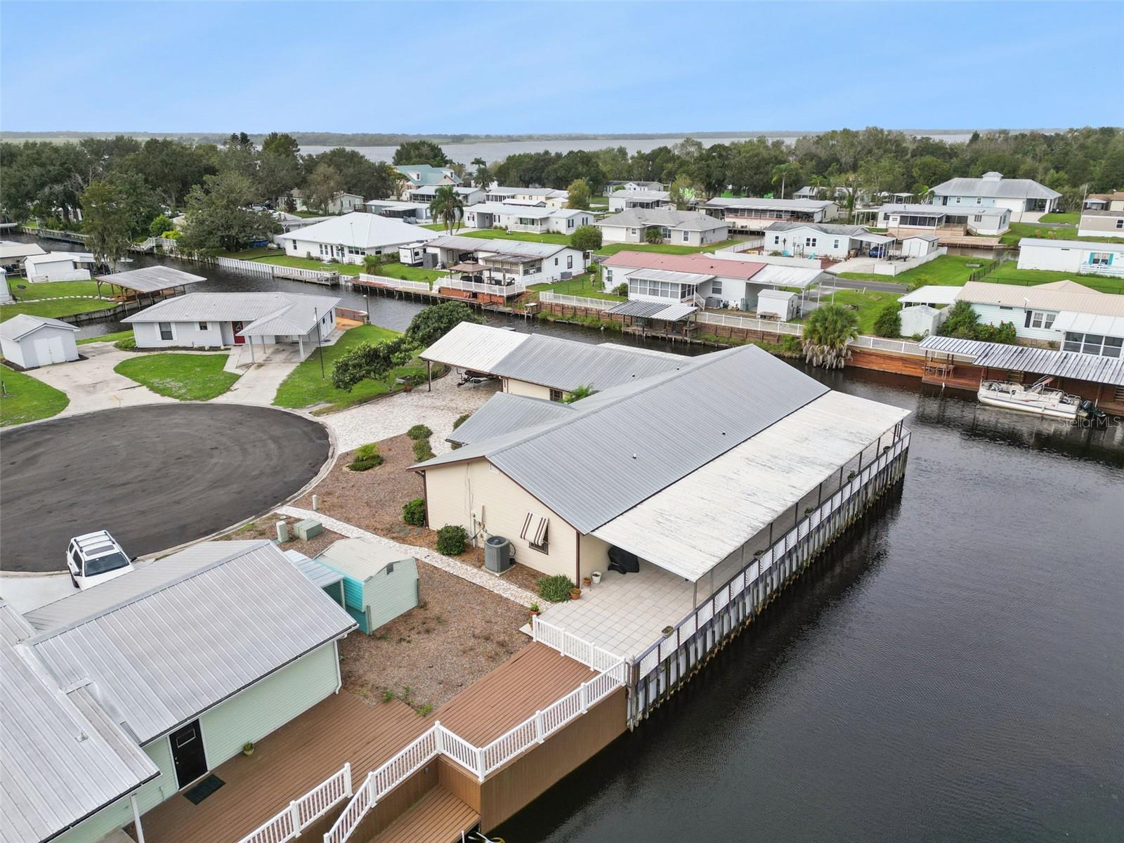Aerial Rear Deck & Canal View: Close-up drone view highlighting the extensive wraparound tiled patio, metal roof structure, and canal seawall